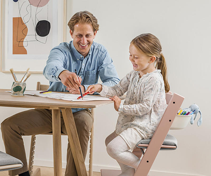 Girl sitting on the Tripp Trapp chair, laughing and painting with her father